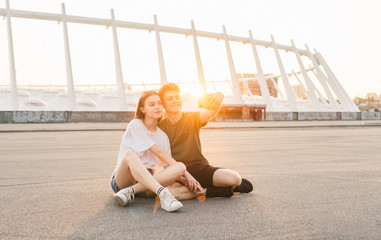 Beautiful happy couple makes photos on the background of the sunset, looking into the camera of a smartphone and smiling.Couple takes a selfie on the background of a beautiful city landscape Lifestyle