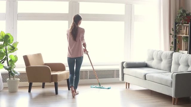 Tidy young woman housewife clean floor in modern living room