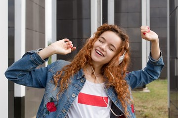 Redhead kinky girl listening to music in big headphones dancing outdoors