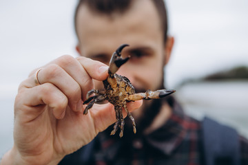 A cool picture of a man who holds a small crab in his arms while walking along the sea in cloudy cold weather