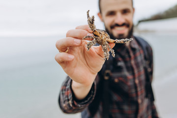 A cool picture of a man who holds a small crab in his arms while walking along the sea in cloudy cold weather
