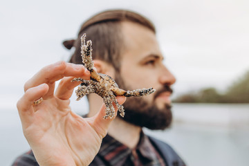 A cool picture of a man who holds a small crab in his arms while walking along the sea in cloudy cold weather