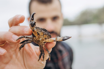 A cool picture of a man who holds a small crab in his arms while walking along the sea in cloudy cold weather