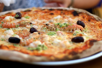 Pizza with tomato sauce, cheese, shrimps, olives and pesto. Selective focus.