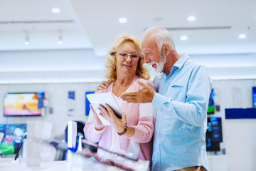Fototapeta premium Happy smiling senior choosing new tablet while standing in tech store.