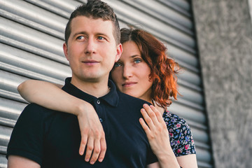 Portrait of a serious young man and woman embracing standing on the background of gray walls