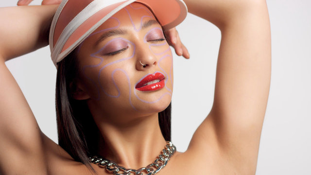 mixed race asian model in studio creative art makeup. Wears a sun cap watching to the camera. Bright creative eye makeup closed eyes
