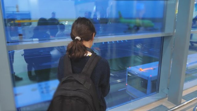daughter with a backpack airplane flights airport concept. girl teenager with a smartphone looks out the window at the airport area lifestyle airplanes and bus at a distance. teen girl looks at the