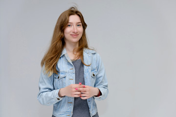 Portrait to waist of a young pretty brunette girl woman with beautiful long hair on a white background in a jacket from jeans. He talks, smiles, shows his hands with emotions in various poses.