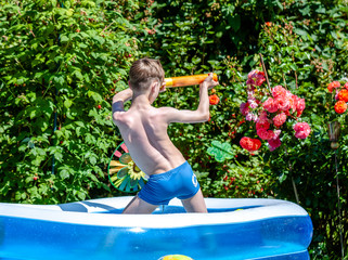 Happy little boy having fun with squirt gun in pool