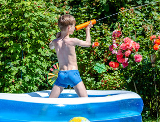 Happy little boy having fun with squirt gun in pool