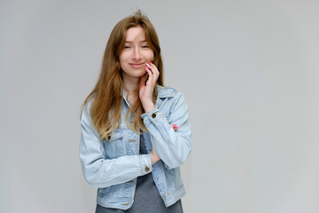 Portrait to waist of a young pretty brunette girl woman with beautiful long hair on a white background in a jacket from jeans. He talks, smiles, shows his hands with emotions in various poses.