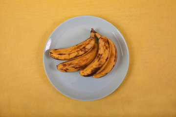 Ugly bananas lie on a blue plate on a yellow background
