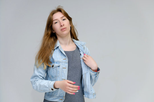 Portrait to waist of a young pretty brunette girl woman with beautiful long hair on a white background in a jacket from jeans. He talks, smiles, shows his hands with emotions in various poses.