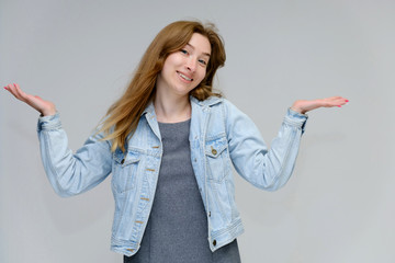 Portrait to waist of a young pretty brunette girl woman with beautiful long hair on a white background in a jacket from jeans. He talks, smiles, shows his hands with emotions in various poses.