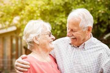 older couple are standing in the garden, hugging each other and laughing at each other