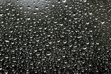 The texture of rain drops on the glass close-up. Macro transparent water drops on dark background.