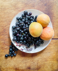 Apricots and black currants on a plate. Fruit from his garden on a wooden table