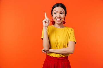 Excited happy young woman posing isolated over orange wall background pointing.
