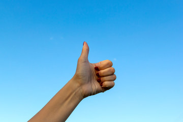 Hand gesturing thumbs up showing good or ok on blue sky background