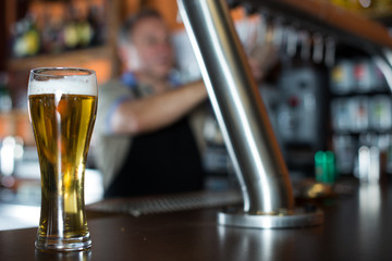 glass of beer on bar counter against background of friendly bartender