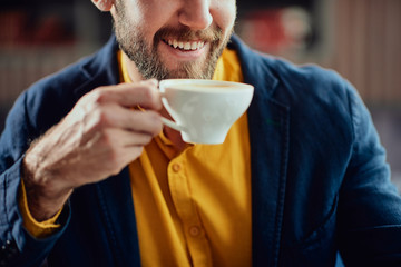 Close up of young Caucasian smiling man drinking coffee in cafe.