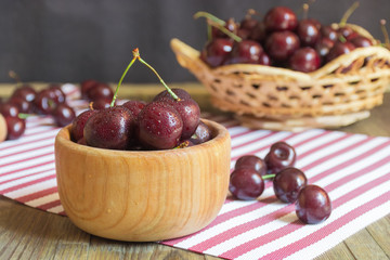 Close up of organic fresh sweet cherries in wooden bowl, farm fruits on farmer market table. Healthy food consept