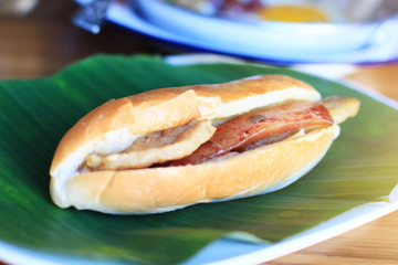Baguette bread sandwich with cheese, ham on fresh Green banana leaf on wooden table in homemade Thai style