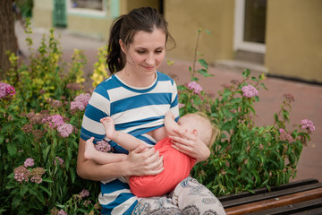young brunete mother breast feeding baby girl outdoors in public town 