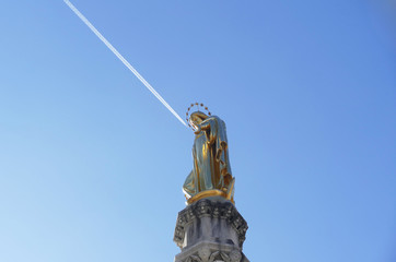 Fototapeta na wymiar Beautiful golden statue of Blessed Virgin Mary high in the blue sky and sign sky 