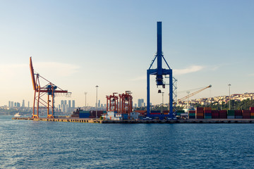 Fototapeta premium Cranes and Containers at container freight station of Haydarpasa Port. View from sea in daytime and city scape on the back.