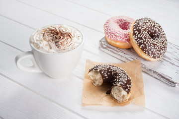 Pink and chocolate donuts with coffee with cream on white wooden table.