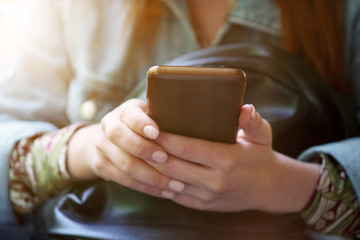 midsection of unrecognizable young woman using her smartphone or mobile phone - trendy filter with sun flare light leak