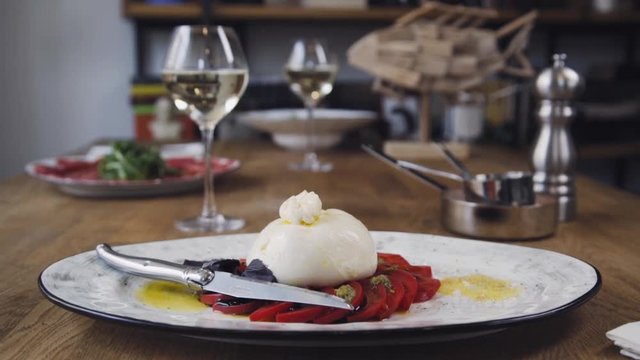 In the restaurant, food and wine are on the table. On the table is a vegetable salad and burrata cheese with tomatoes. Burrata cheese stands on a wooden table in a cafe.