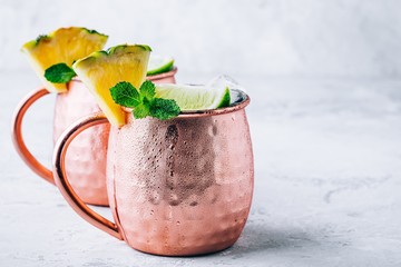 Iced Cold Moscow Mule cocktail with lime and pineapple on dark background