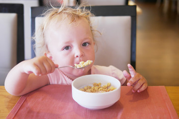 Little baby eats yogurt from a cup in a restaurant.