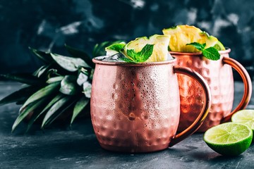 Iced Cold Moscow Mule cocktail with lime and pineapple on dark background