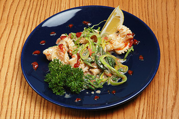 Steamed vegetables with seafood on a blue plate on a wooden background