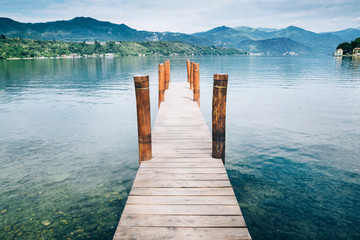 Wooden pier on Orta San Giulio Lake with greenery mountain background. Italy.