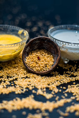 Curd or yogurt and oats face mask on the woodne surface in a glass bowl along with some raw oats in a black colored clay bowl and some spread on the surface. To Exfoliate Your Skin.