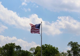The american flag over the treetops and the cloud in sky.