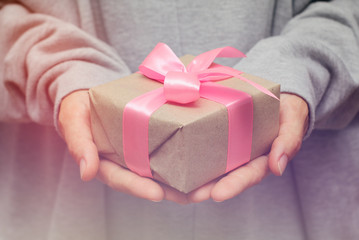 Hand hold the gift box. Present wrapped in craft paper and satin ribbon. Small parcel in a girls hands. Christmas time. 