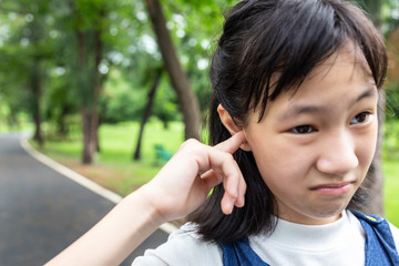 Portraits of asian little girl stressed putting a finger in to her ear,annoyed expression,closeup of cute child having any itchiness,rash using finger to scratching ear in outdoor park