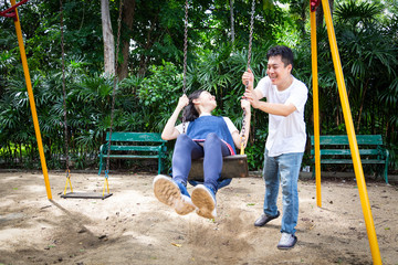 Happy asian child girl having fun,enjoy,playful,playing on the swing,beautiful daughter riding on swing in playground,smiling father pushing,dad swinging her in outdoor park,vacation family concept