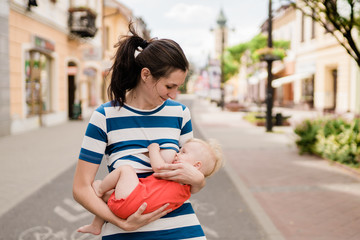 young brunete mother breast feeding baby girl outdoors in public town 