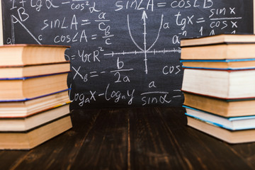 Books on a wooden table, against the background of a chalk board with formulas. Teacher's day concept and back to school.