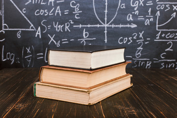 Books on a wooden table, against the background of a chalk board with formulas. Teacher's day concept and back to school.