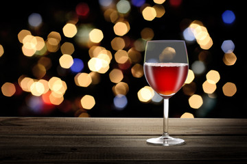 red wineglass on a wooden table with night party bokah lights on the backgroung and copy space for your text