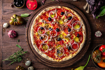 Tasty hot italian pizza Mexicana with Pork, Mozzarella, Pepperoni, Pickled Cucumbers, Olives, Tomatoes, Red Onions, Stewed Onions, Tomato Sauce  on old wooden table. Pizzeria menu. 