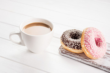 Pink and chocolate donuts with coffee with cream on white wooden table.